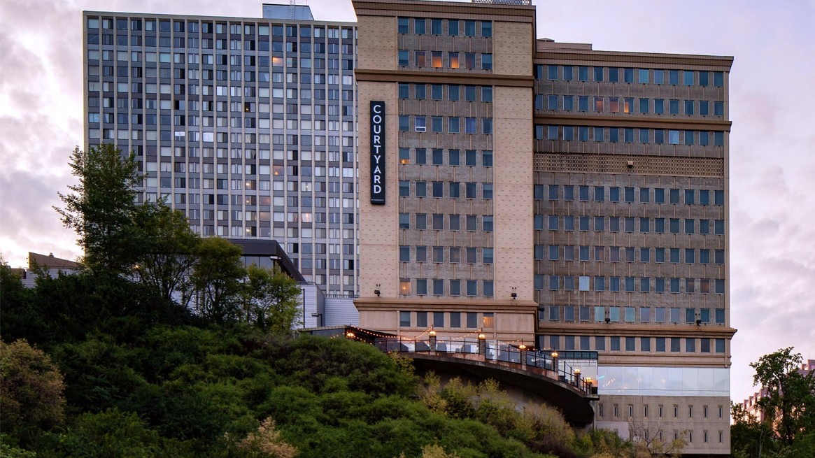 Courtyard by Marriott hotel perched on a hillside with trees in the foreground and a vertical sign on the facade reading COURTYARD.