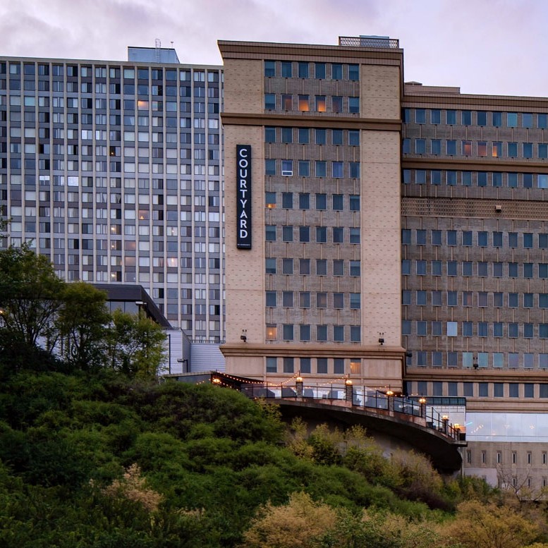 Courtyard by Marriott hotel perched on a hillside with trees in the foreground and a vertical sign on the facade reading COURTYARD.
