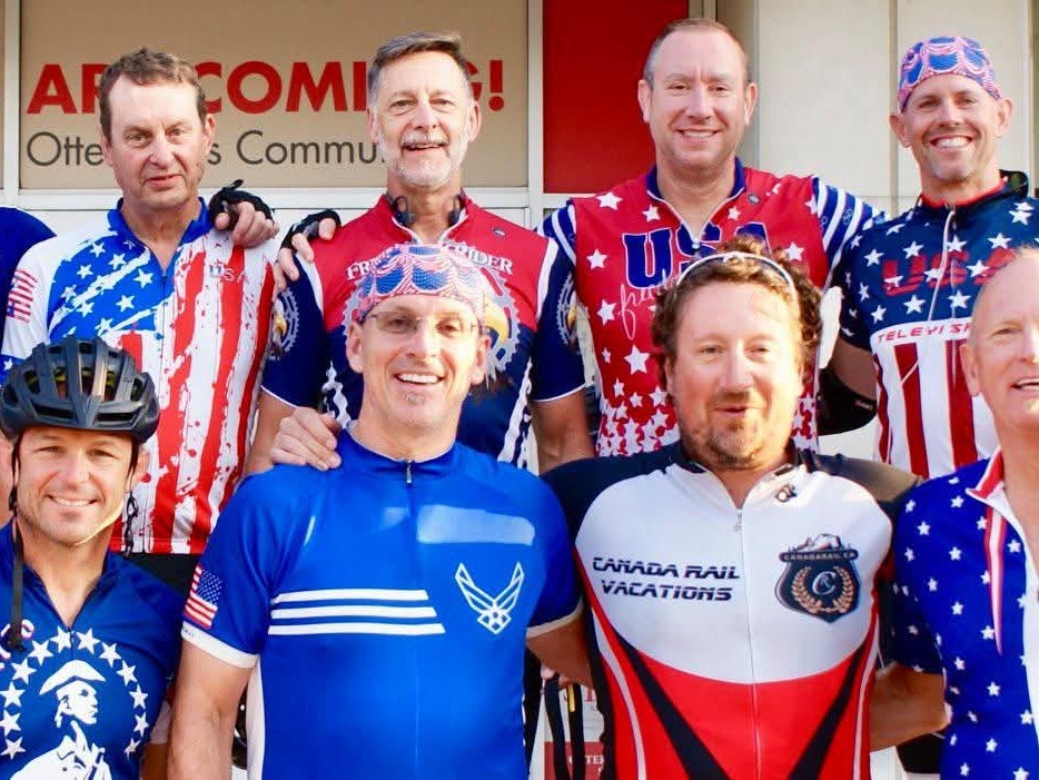 Group of men in red, white, and blue cycling jerseys posing together for a photo outside a building.
