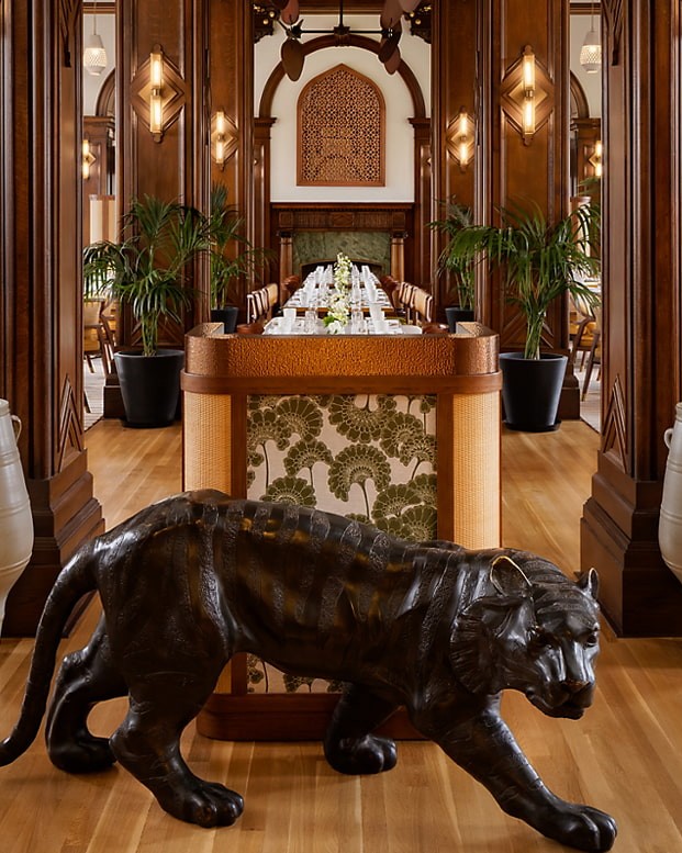 Decorative black tiger sculpture prowling on a polished wooden floor in an upscale restaurant hall with long dining tables and warm lighting.